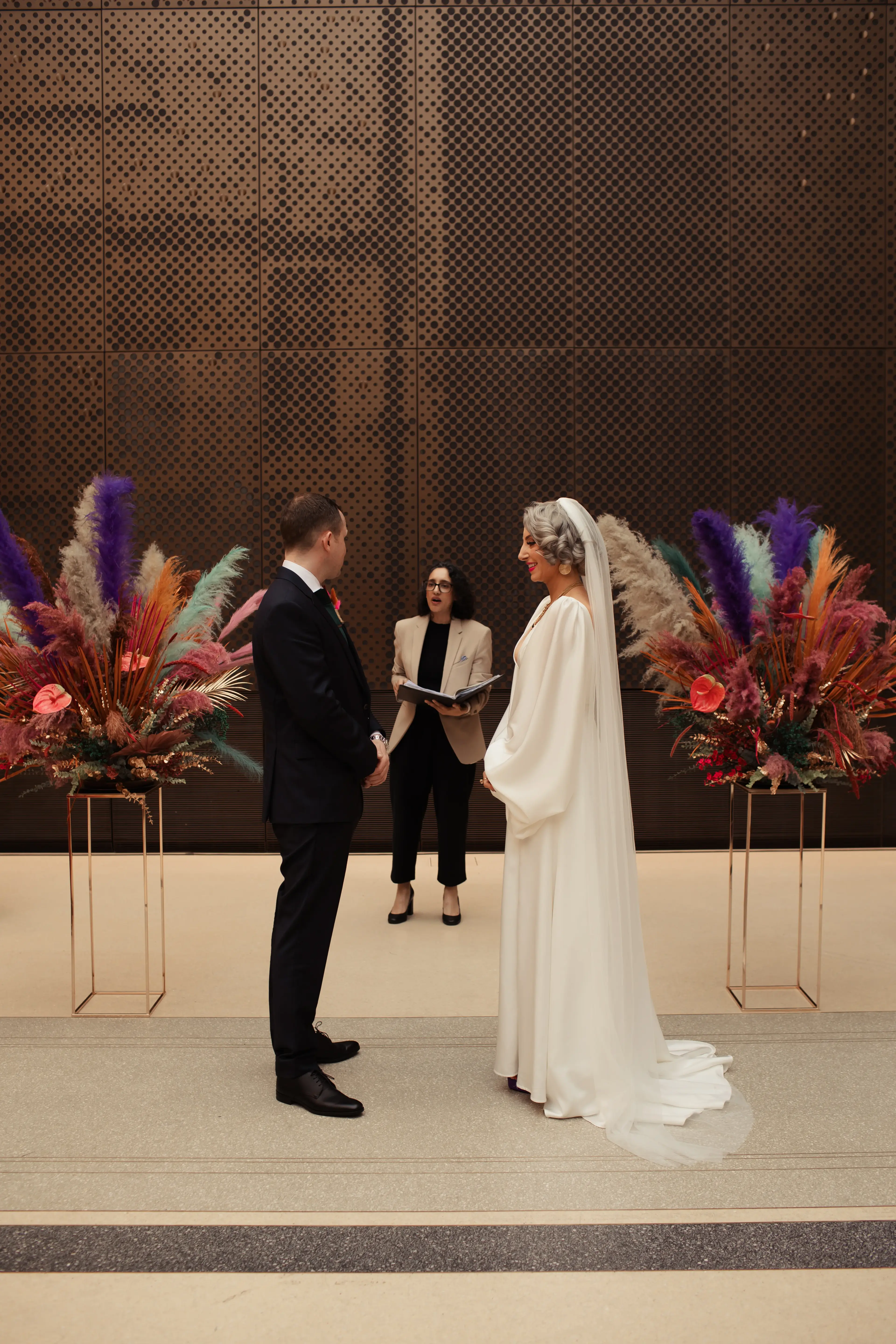 Bride and groom in front of colourful floral decorations for their wedding ceremony at Hackney Town Hall