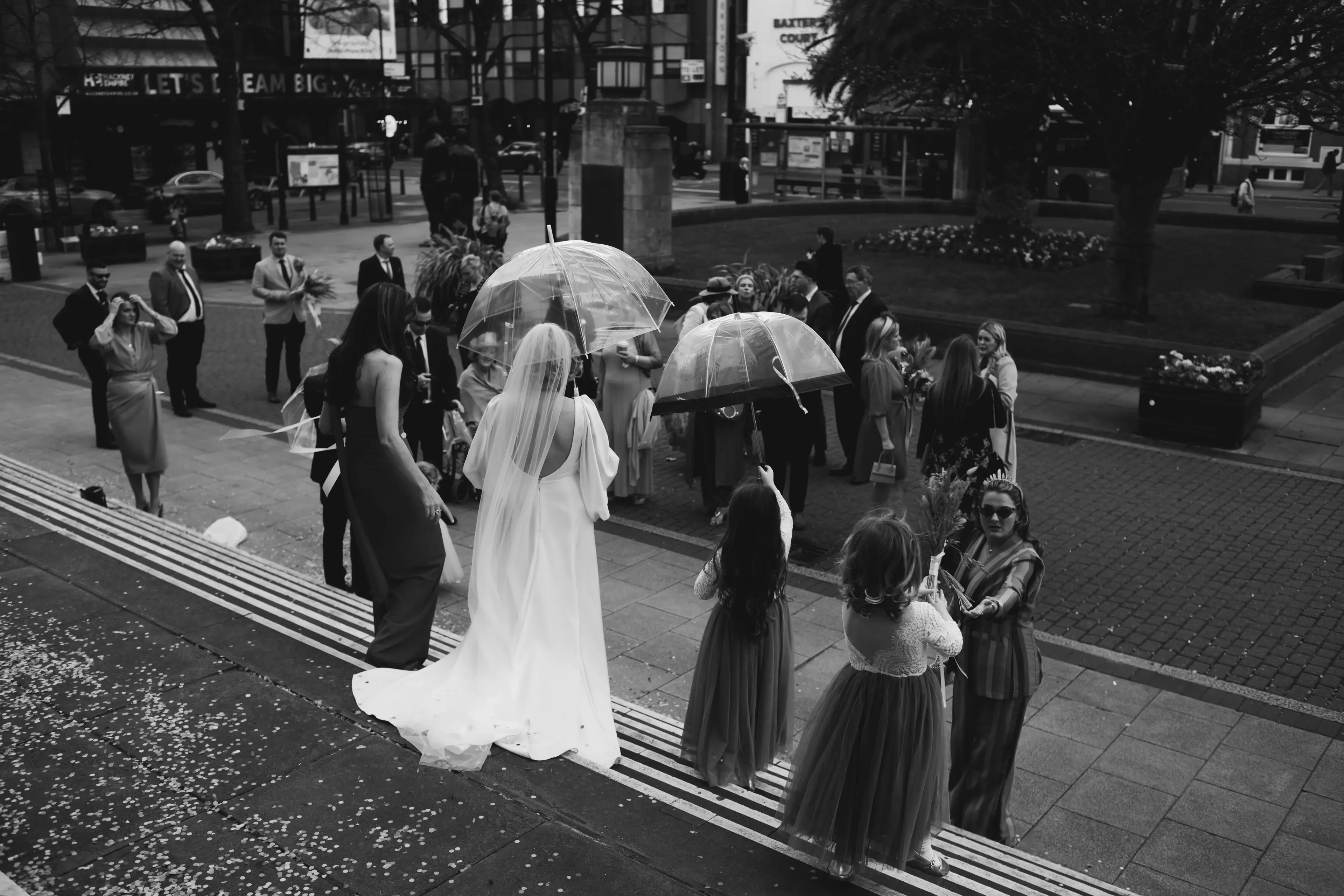 Bride holding an umbrella with some guests gathered outside Hackney Town Hall, London