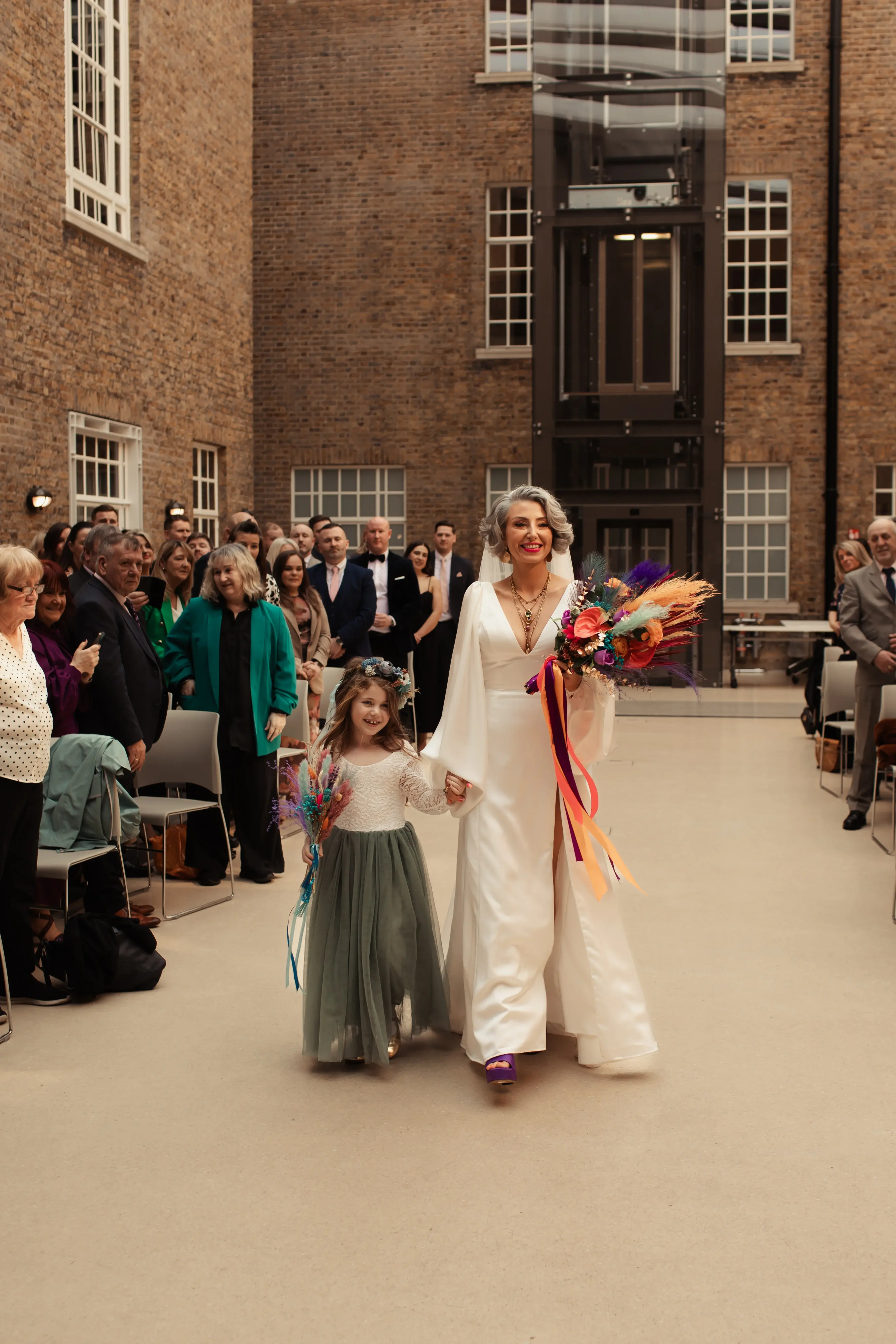 A bride walking down the aisle for her wedding with a flower girl at Hackney Town Hall