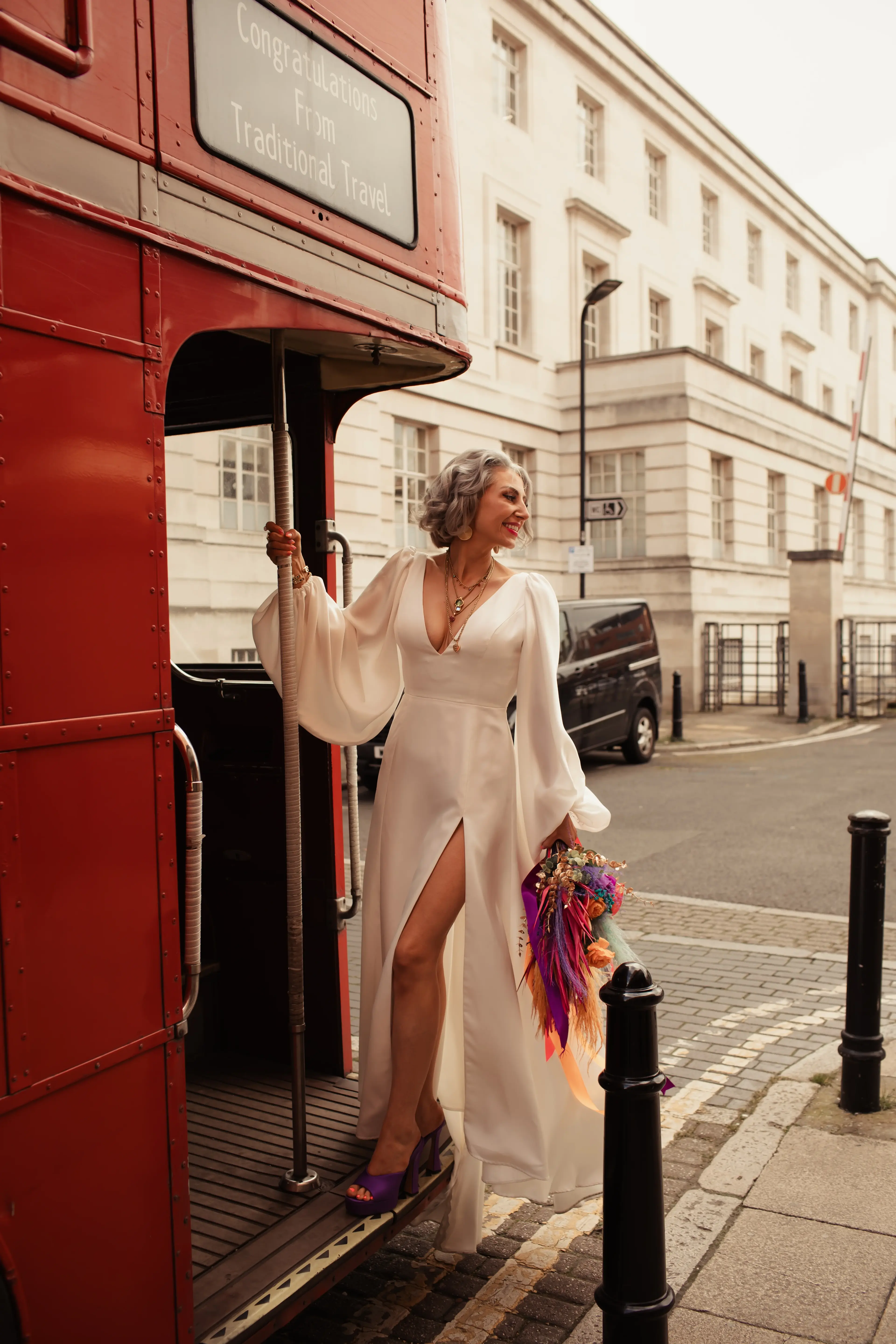 A newly married bride stood on the back of a London red bus with a colourful floral bouquet