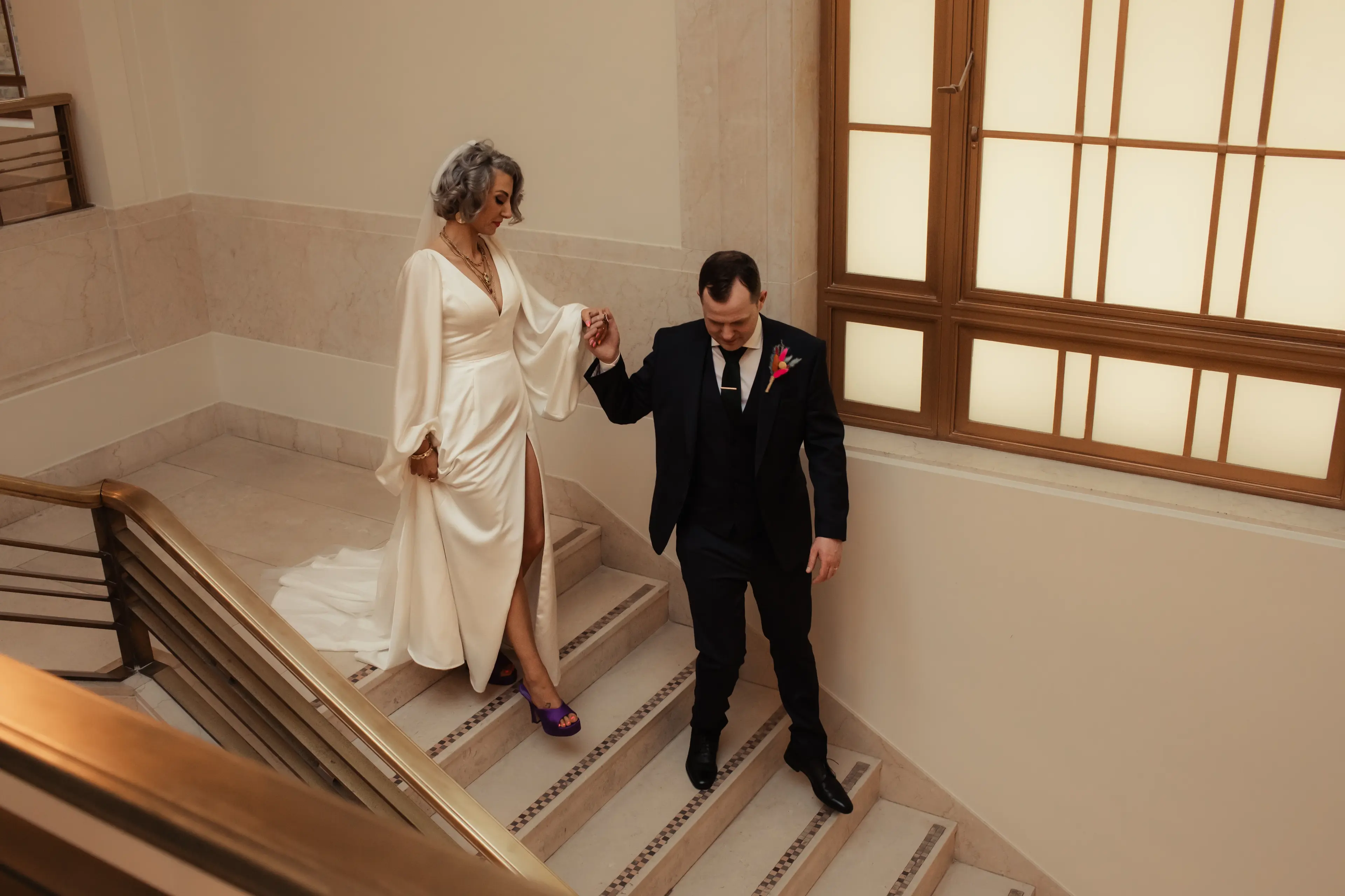 Newly married groom leading his bride down some stairs in Hackney Town Hall